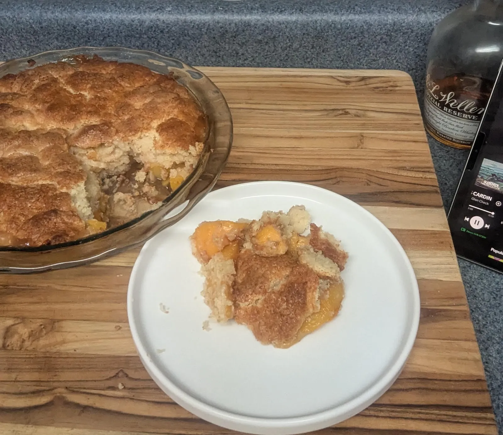 Bourbon peach cobbler in a baking dish with a serving on a plate