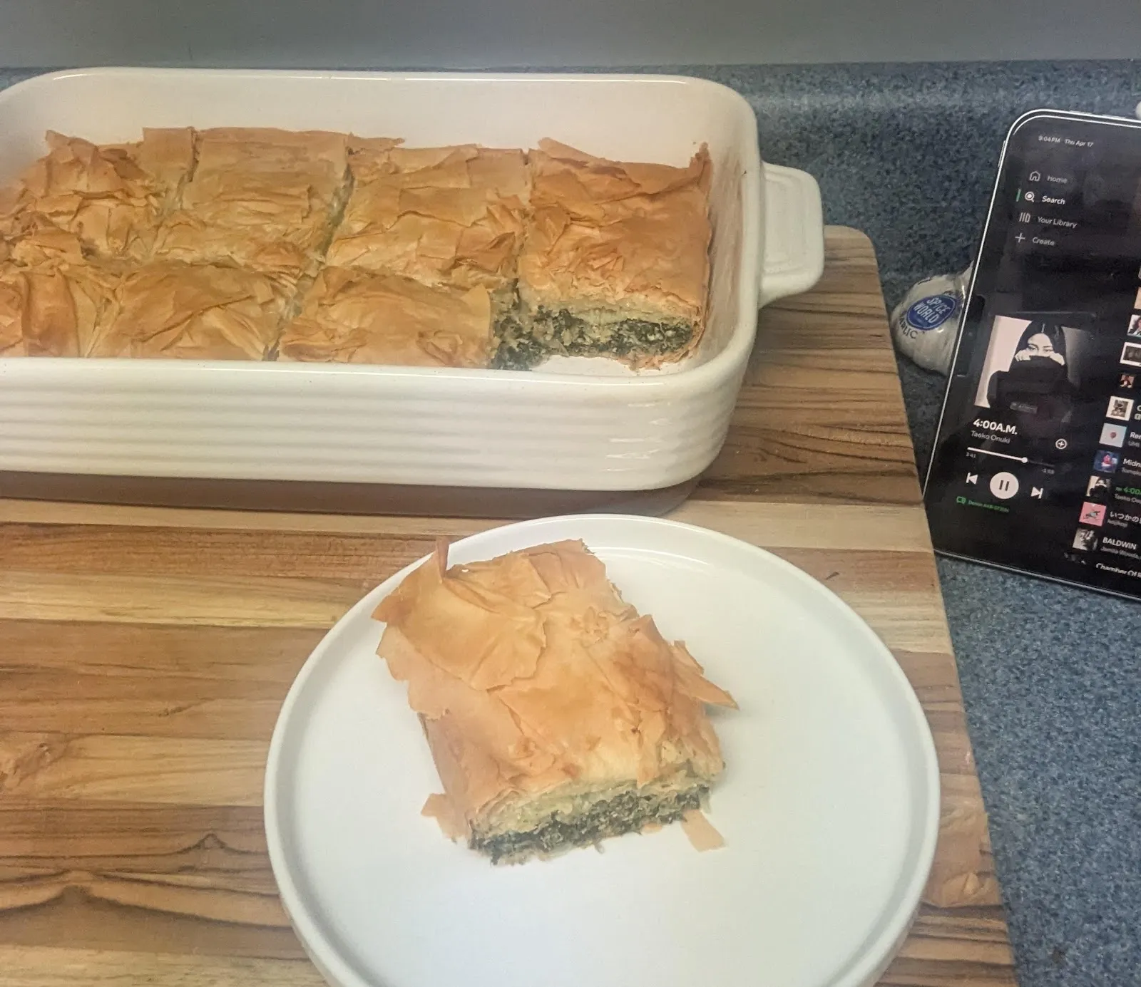 A square of flaky spanakopita in front of the full baking dish