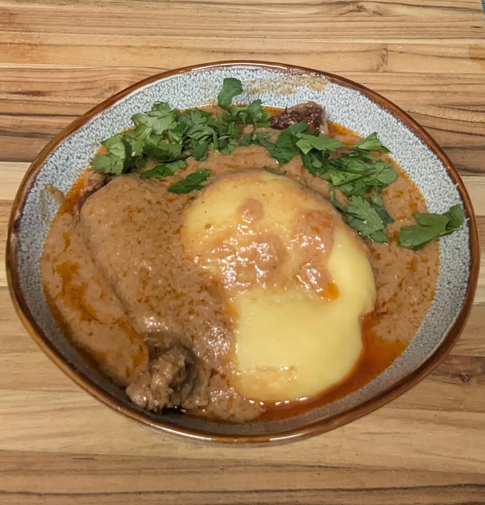 A bowl of groundnut soup with chicken around a mound of fufu