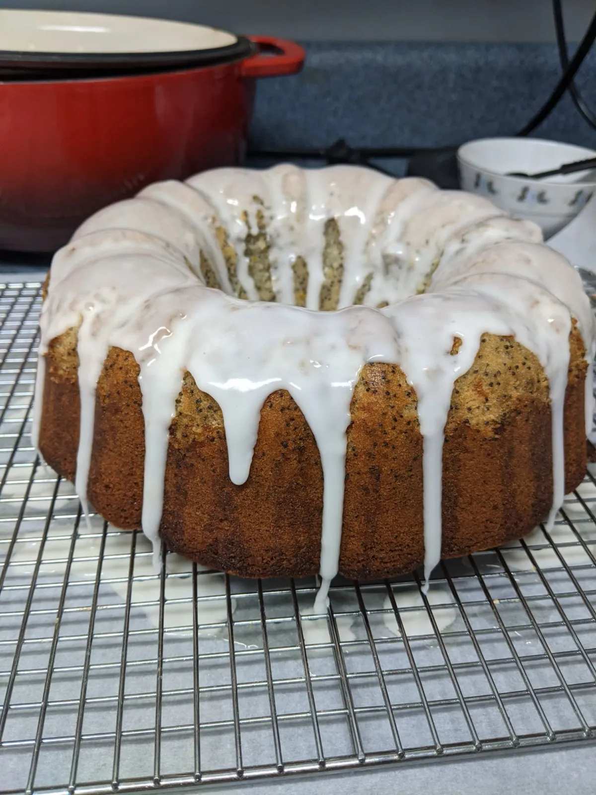 A lemon poppy seed bundt cake on a cooling rack, dripping with thick white lemon glaze